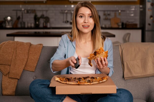 Mulher comendo pizza enquanto assiste tv