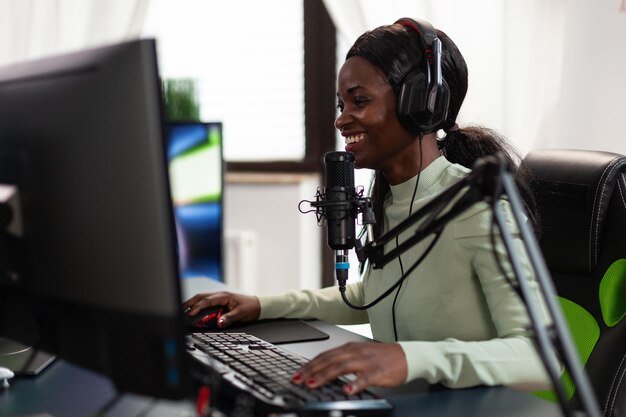 Mulher competitiva de cyber gamer falando no microfone com jogadores em transmissão ao vivo enquanto joga videogames de tiro espacial durante torneio online usando equipamento de computador RGB. E competição esportiva