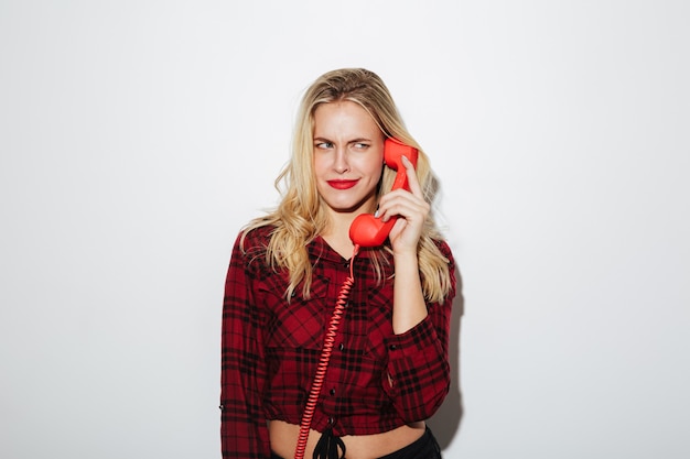 Mulher confusa falando pelo telefone retrô vermelho.