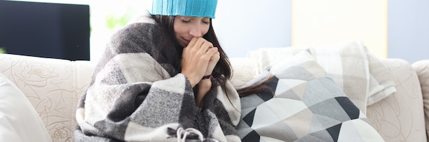 Mulher congelada com chapéu e cobertor sentada no sofá
