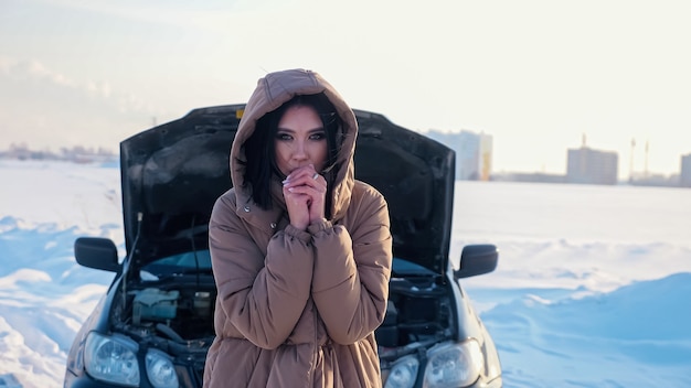 Mulher congelada em uma jaqueta quente perto de um automóvel quebrado Foto Premium
