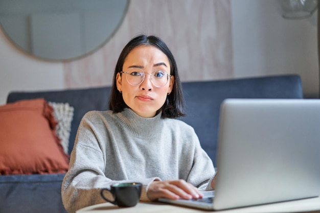 Mulher coreana com rosto perplexo sentado com laptop trabalhando em freelancer remoto com expr confuso