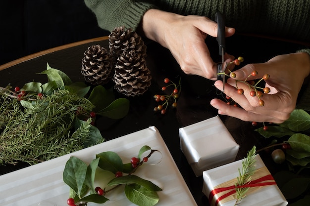 Mulher cortando pedaços de plantas para decorar presentes de natal, com espaço de cópia.