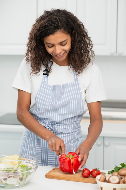 Mulher cortando uma pimenta vermelha na cozinha