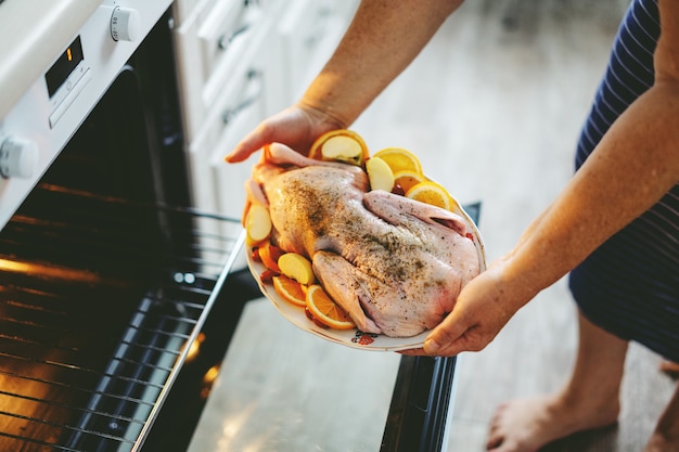 Mulher cozinhando pato de Natal, colocando pato cru com legumes no forno.