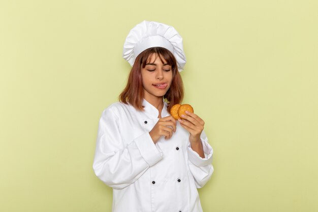 Mulher cozinheira de terno branco comendo biscoitos na superfície verde