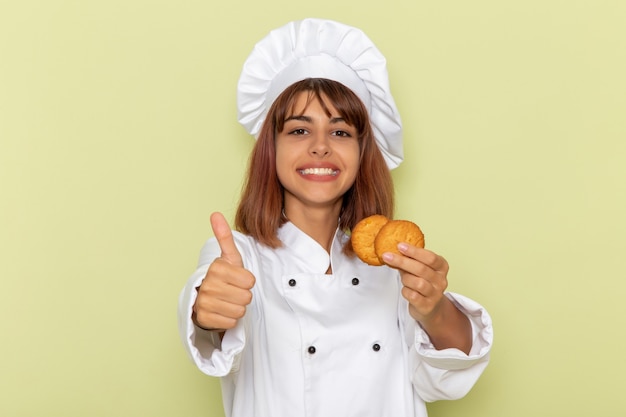 Mulher cozinheira de terno branco segurando biscoitos de açúcar sobre uma superfície verde