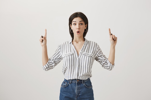 Foto grátis mulher curiosa e bonita apontando o dedo para o anúncio, promover o produto