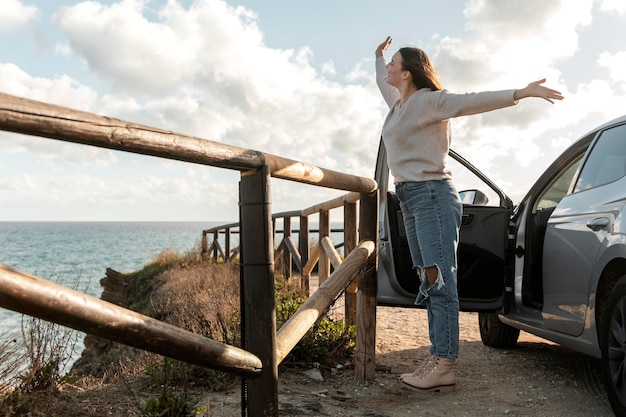 Mulher curtindo a brisa da praia ao lado do carro