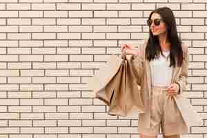 Foto grátis mulher da moda segurando sacolas de compras cópia espaço parede de tijolos