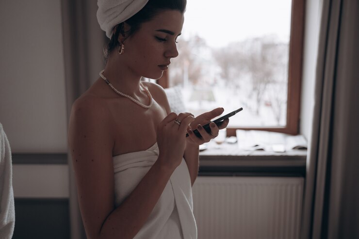 Foto grátis mulher de beleza em um roupão de banho e com uma toalha na cabeça usando smartphone