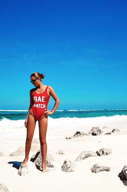 Mulher de biquíni vermelho posando na praia de verão atrás do céu azul e mar