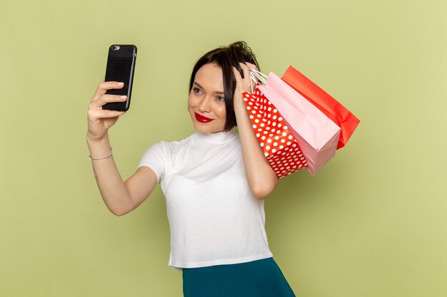 mulher de blusa branca e saia verde segurando pacotes de compras, tirando uma selfie