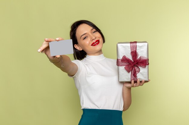 mulher de blusa branca e saia verde segurando um cartão cinza e uma caixa de presente