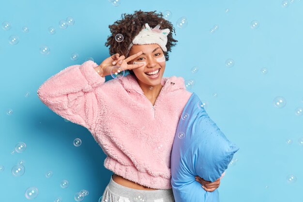 Mulher de cabelo encaracolado bonita e positiva faz um gesto de vitória sobre um sorriso largo