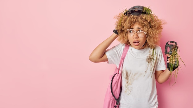 Foto grátis mulher de cabelo encaracolado envergonhada se prepara para a maratona de bicicleta quebrou a bicicleta tenta resolver o problema carrega a trava da bolsa de tecido e o pedal parece espantado isolado sobre o espaço de cópia de fundo rosa