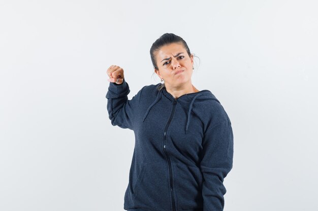 Mulher de cabelo escuro e casaco levantando o braço de forma agressiva