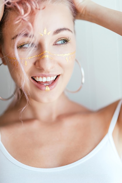 Mulher de cabelo rosa e maquiagem artística em forma de pinceladas sorrindo à parte, posando em branco claro