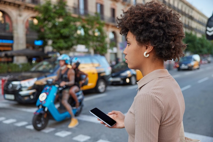 Foto grátis mulher de cabelos cacheados cruza uma rua movimentada com um smartphone moderno com poses de tela de maquete em branco ao ar livre