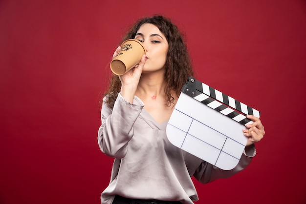 Foto grátis mulher de cabelos cacheados segurando claquete e bebendo café.