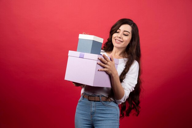 Mulher de cabelos compridos segurando caixas de presentes em fundo vermelho. Foto de alta qualidade