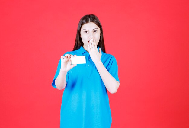 mulher de camisa azul, apresentando seu cartão de visita e ficando surpresa e apavorada.