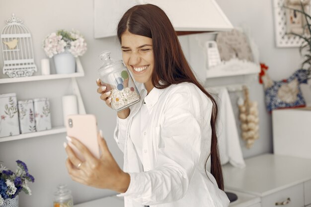 Mulher de camisa branca em pé na cozinha e fazendo uma selfie