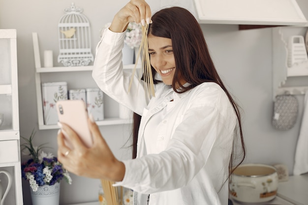 Mulher de camisa branca em pé na cozinha e fazendo uma selfie