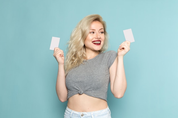 Mulher de camisa cinza e jeans azul brilhante segurando cartões brancos