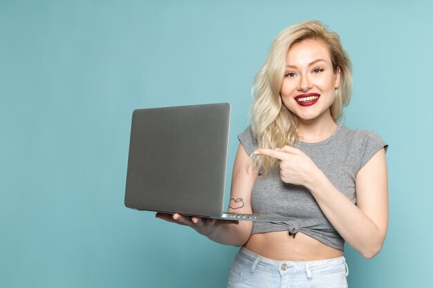 Mulher de camisa cinza e jeans azul brilhante segurando um laptop