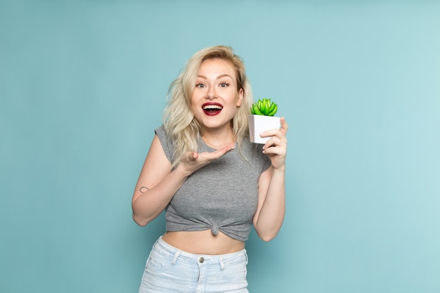 mulher de camisa cinza e jeans azul brilhante segurando uma plantinha