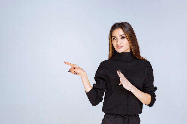 mulher de camisa preta, apontando para a esquerda e mostrando suas emoções.