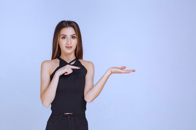 Mulher de camisa preta, apresentando algo na mão.