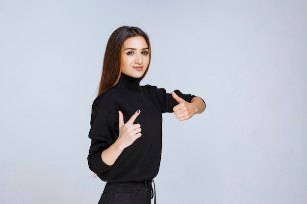 mulher de camisa preta, mostrando sinal positivo com a mão.