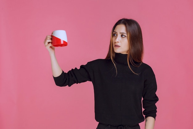 Mulher de camisa preta segurando uma xícara de café e sorrindo.