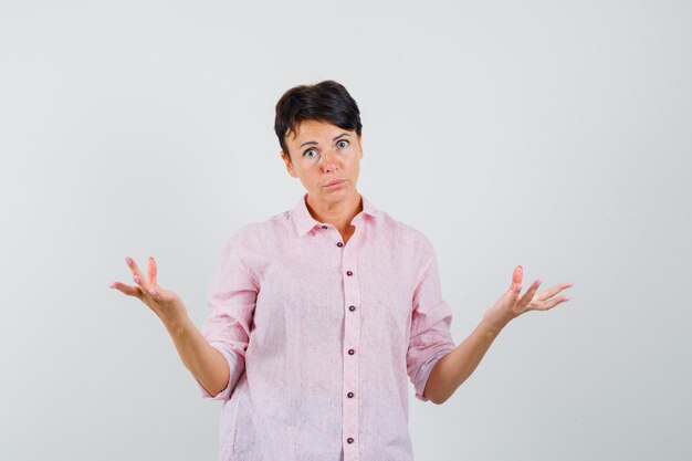 Mulher de camisa rosa, mostrando um gesto desamparado e parecendo confusa, vista frontal.