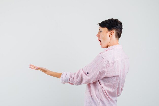 Mulher de camisa rosa, segurando a palma da mão e parecendo animada.