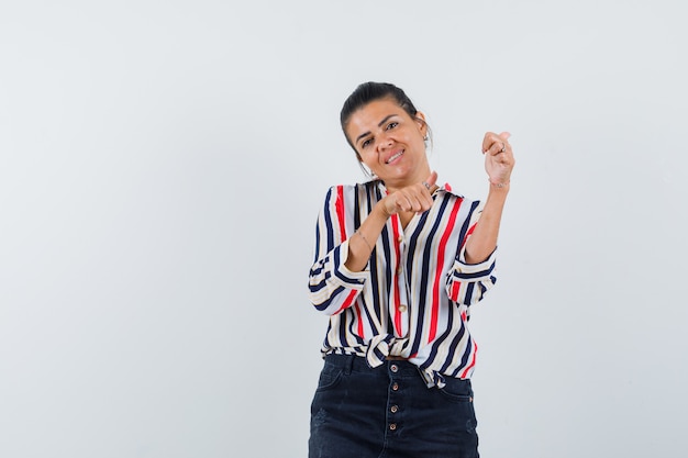 Mulher de camisa, saia apontando para trás com polegares e parecendo alegre