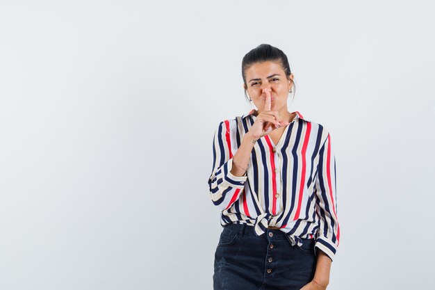 mulher de camisa, saia mostrando gesto de silêncio e parecendo confiante