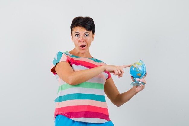 Mulher de camiseta listrada, calça segurando o dedo no modelo globo e parecendo surpresa