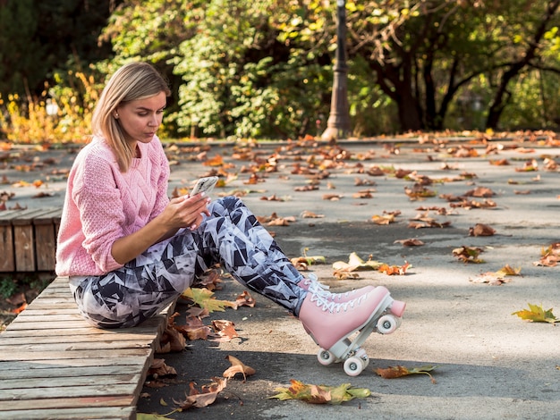 Mulher de caneleiras e patins segurando o smartphone com espaço de cópia