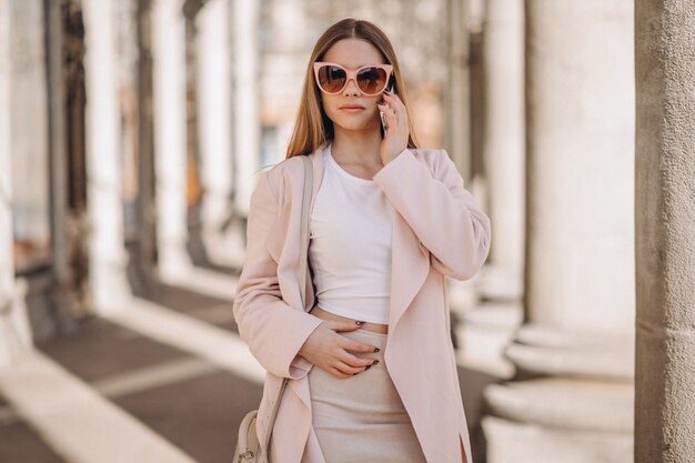 Mulher de casaco andando na rua e falando ao telefone