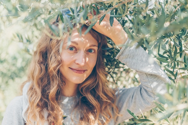 Mulher de casaco cinza segurando ramo e sorrindo na natureza durante o dia