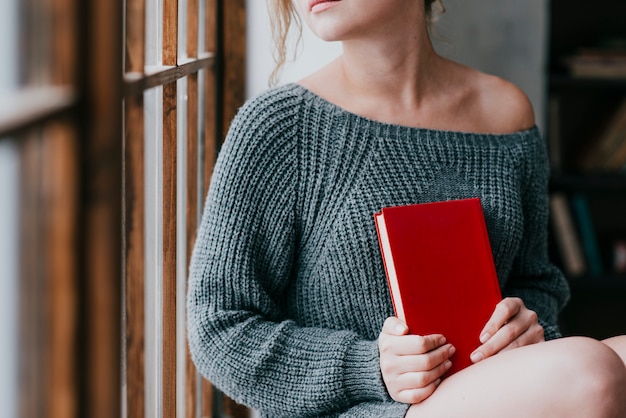 Mulher de colheita com livro sentado perto da janela