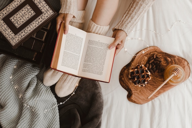 Mulher de colheita lendo livro perto de waffle e mel