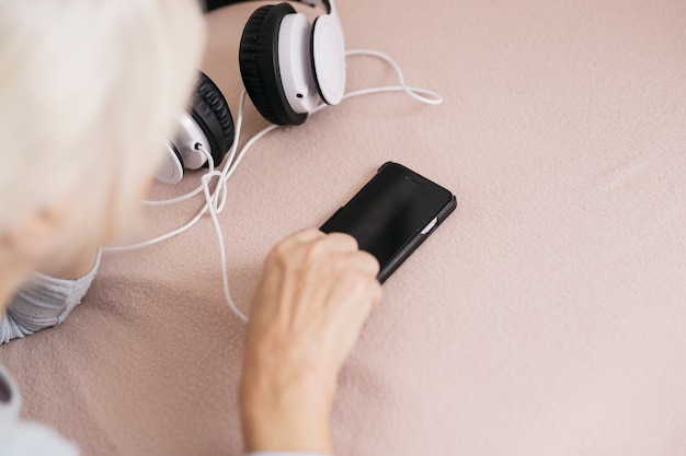 Mulher de colheita usando smartphone perto de fones de ouvido