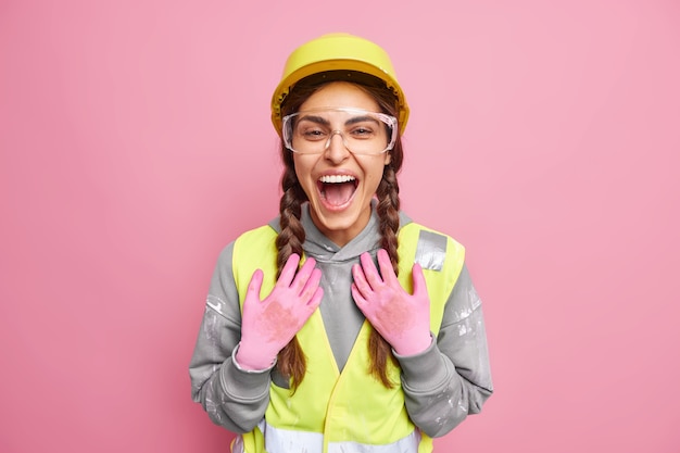 Mulher de construção alegre se prepara para reconstrução edifício inspeciona local usa óculos de proteção, chapéu, luvas, ri positivamente satisfeita com os resultados do trabalho. manutenção da ocupação do trabalho.