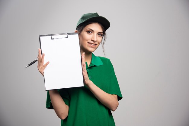 Mulher de entrega de uniforme verde, segurando a prancheta.