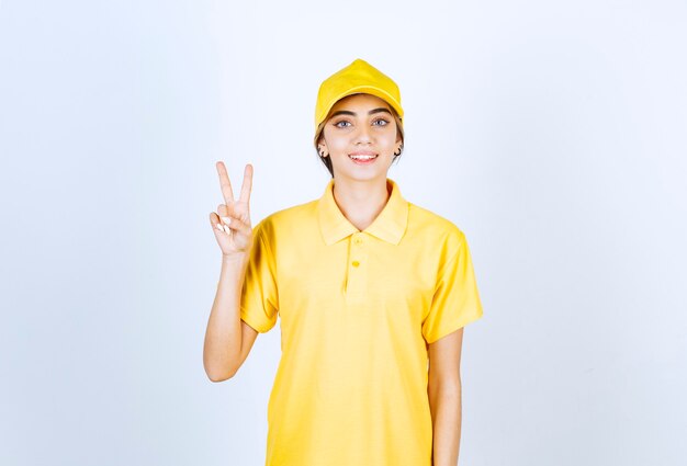 Mulher de entrega em uniforme amarelo em pé e mostrando sinal de vitória.