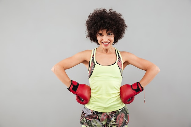 Mulher de esportes sorridente em luvas de boxe, segurando os braços nos quadris